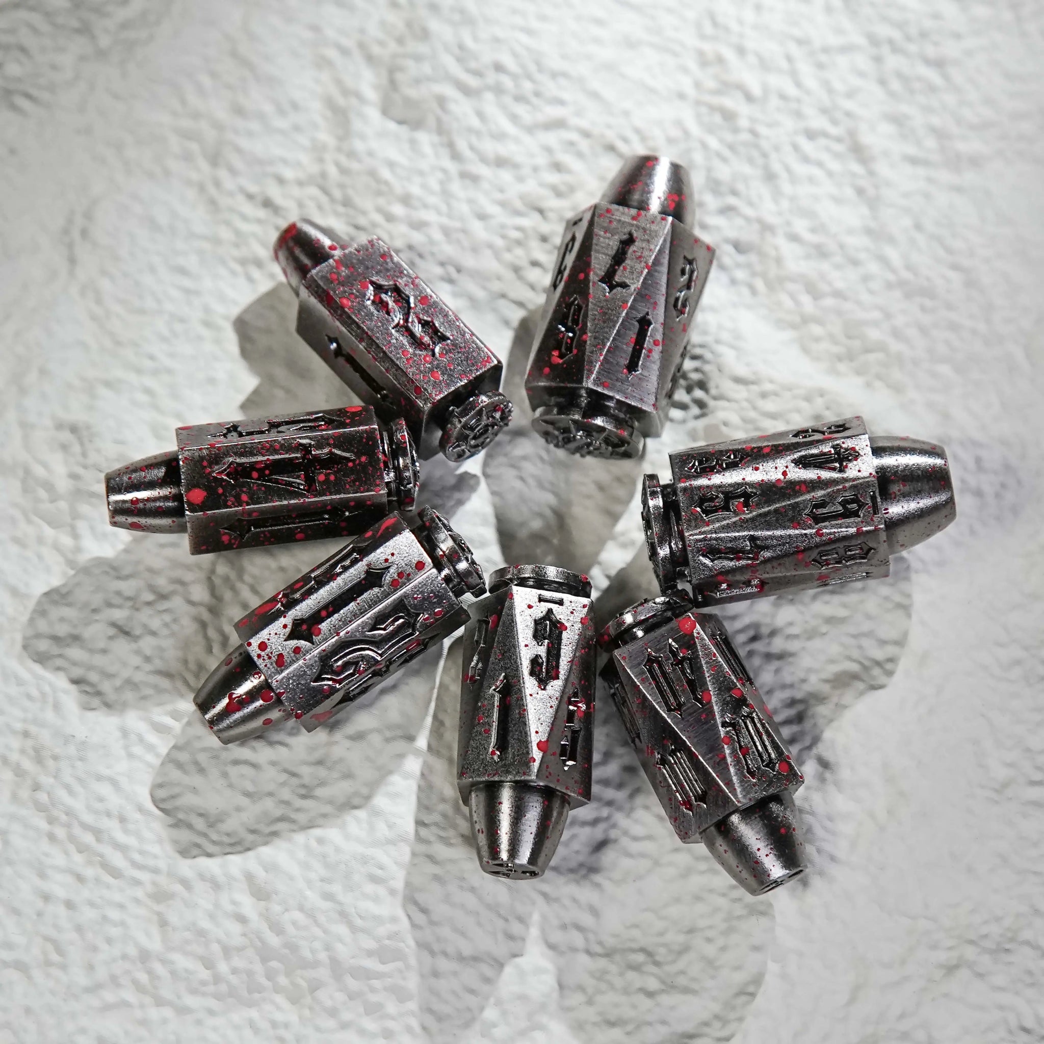 A cool set of bloodstained polyhedron DND silver metal bullet dice are placed in a circle on the table. Unique bullet-shaped RPG dice | Bear Dice