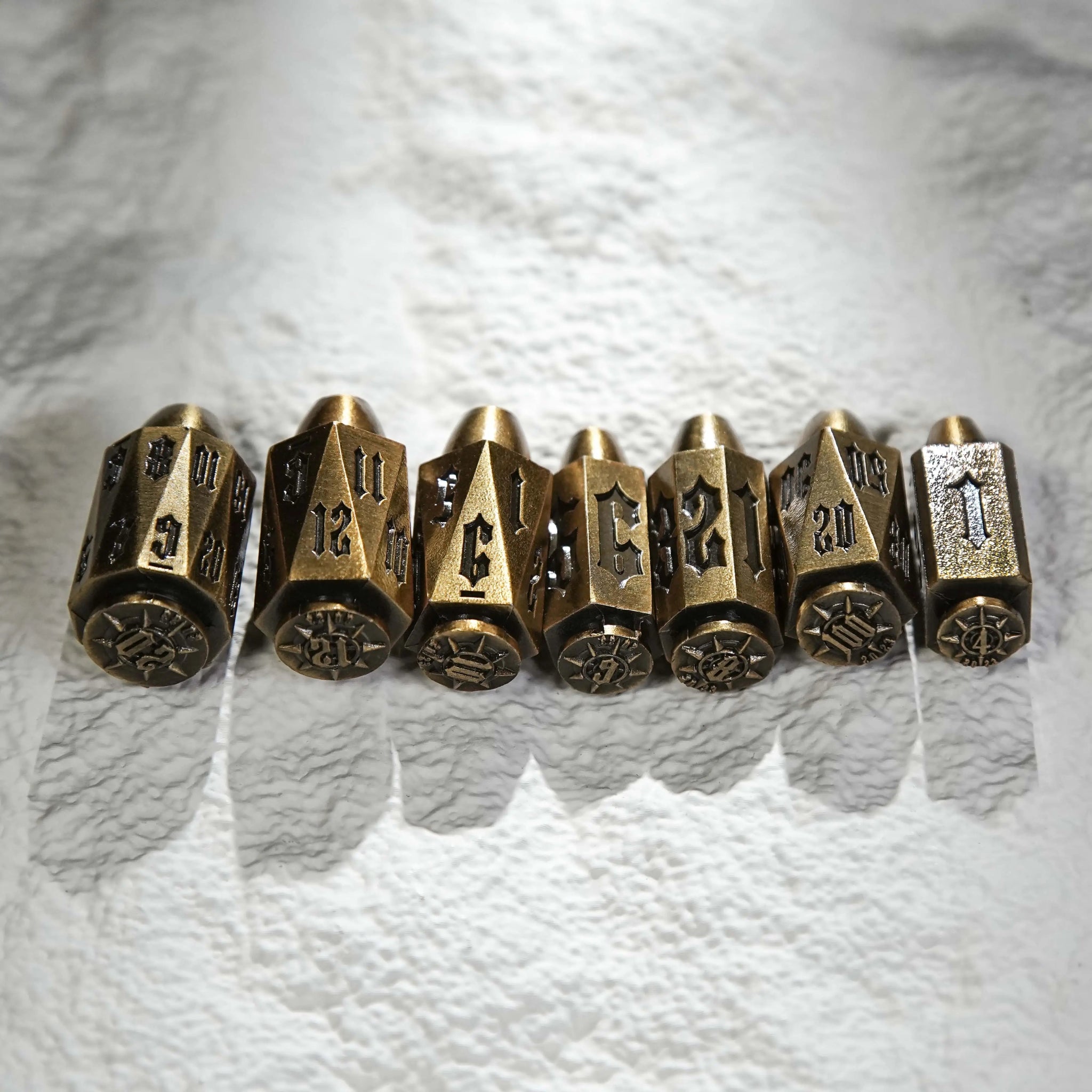 Cool antique gold polyhedron DND metal bullet dice set lined up on the table, unique bullet-shaped RPG dice | Bear Dice