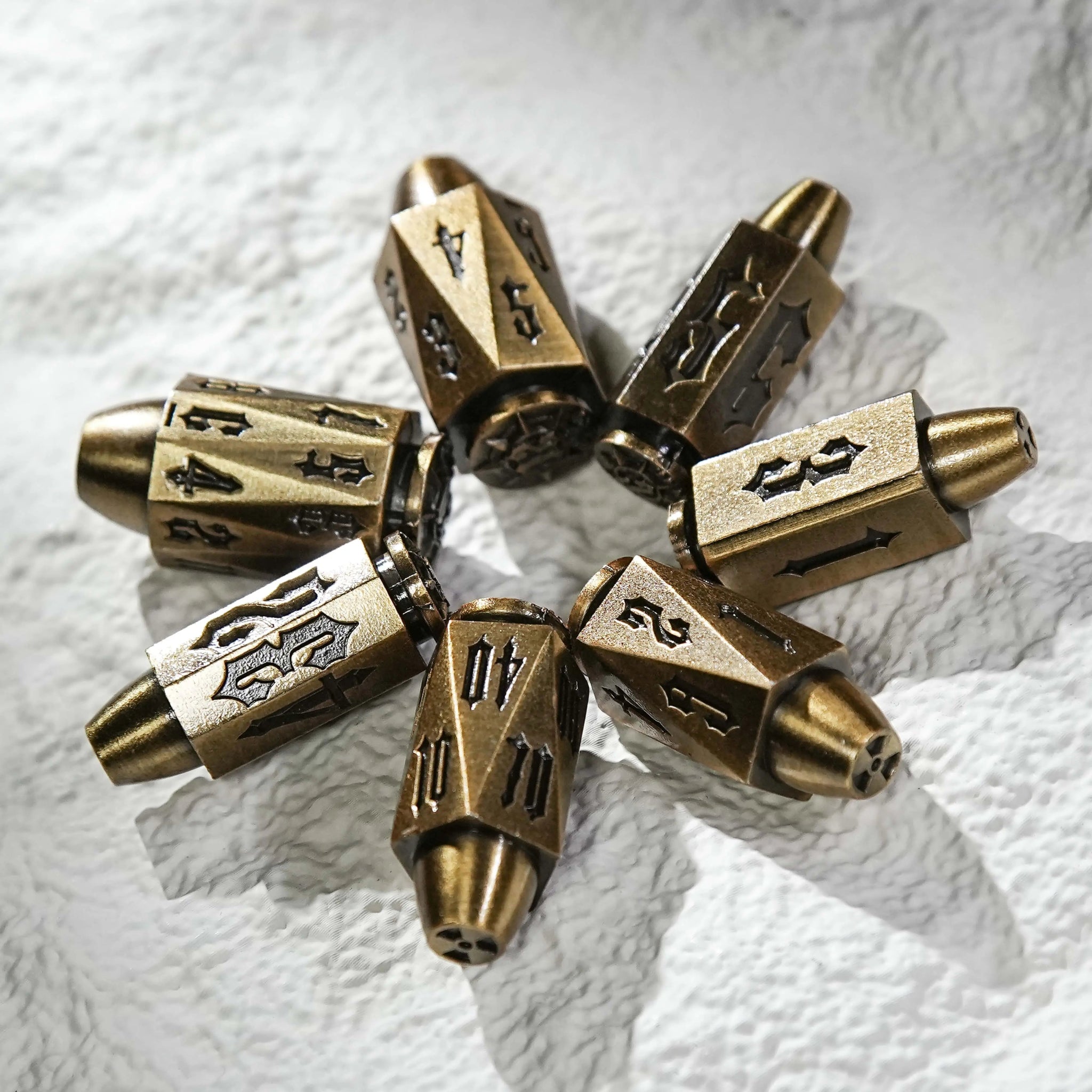 Cool antique gold polyhedron DND metal bullet dice, arranged in a circle on the table. Unique bullet-shaped RPG dice | Bear Dice