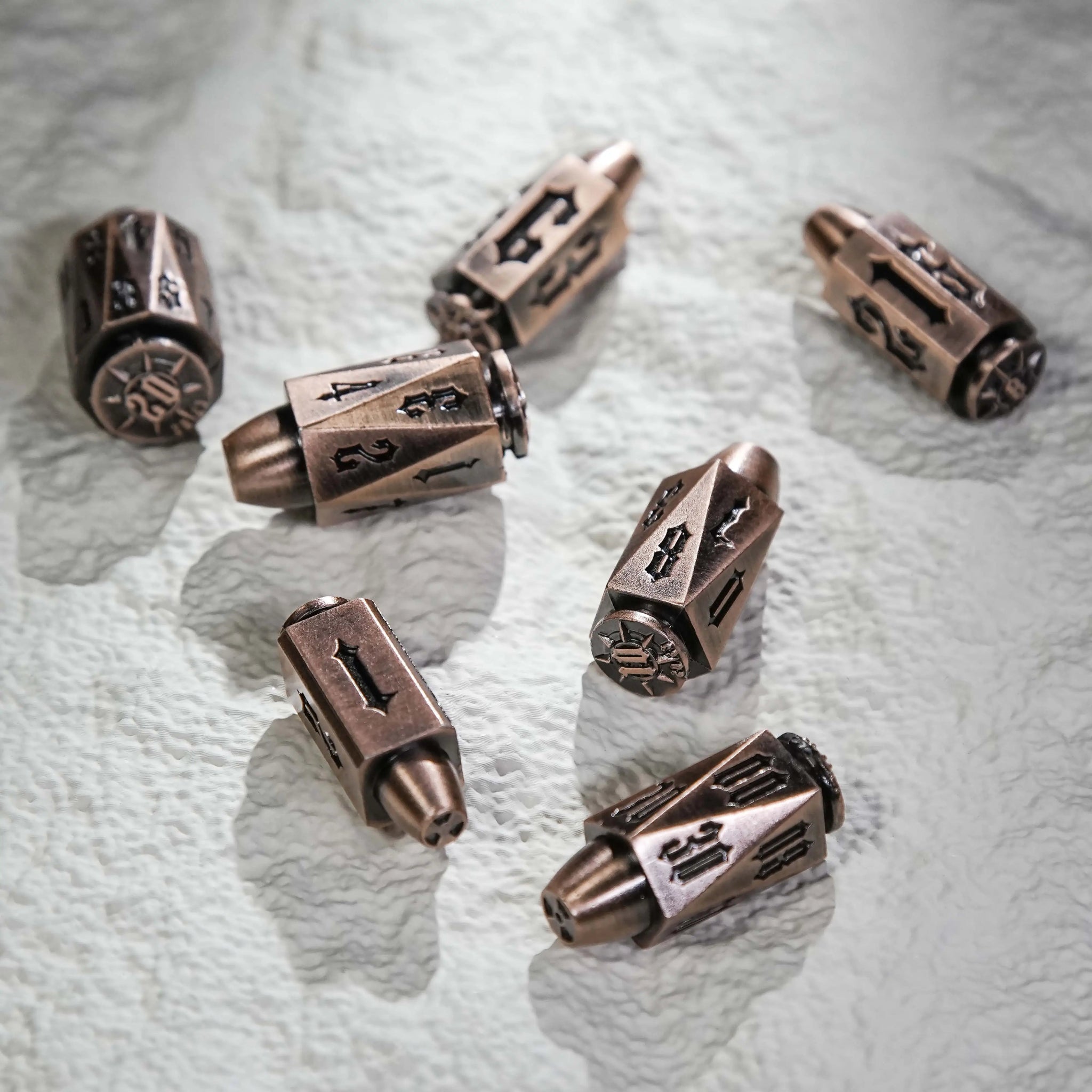 Cool DND dice: Copper Polyhedron Metal Bullet Dice Set scattered on a white table, along with bullet-shaped RPG dice | Bear Dice