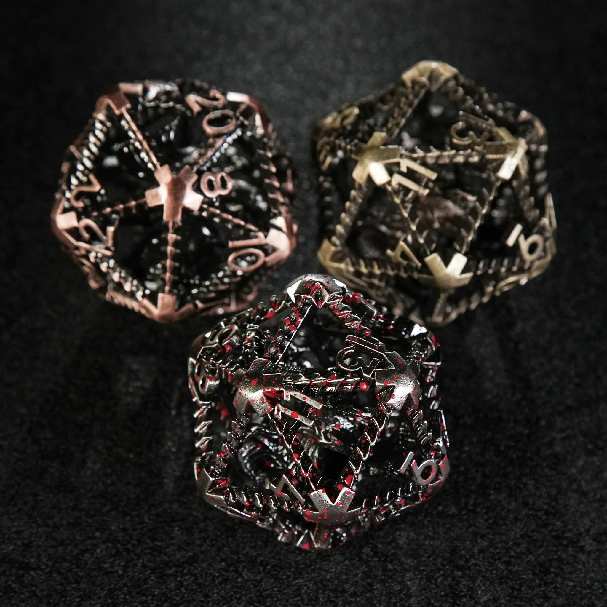 Three large 40mm metal hollow dragon D20 dice (blood, copper, and bronze) placed on a black table | Bear Dice