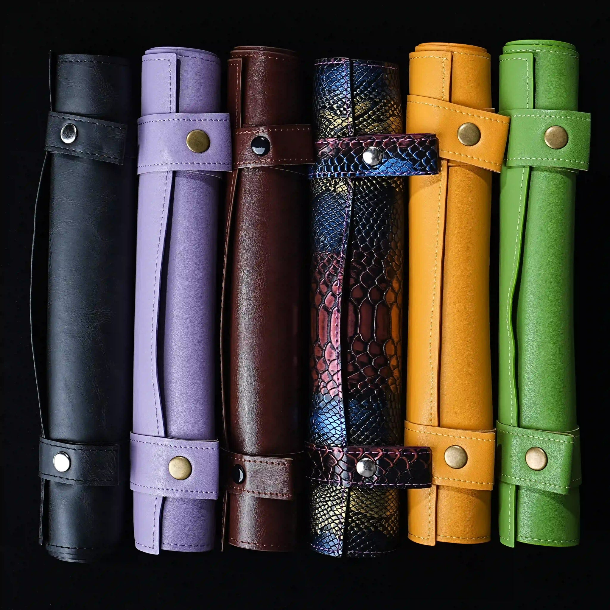 Six leather dice mats and trays in black, crimson, snakeskin, orange, green, and light purple, neatly arranged in a row | Bear Dice