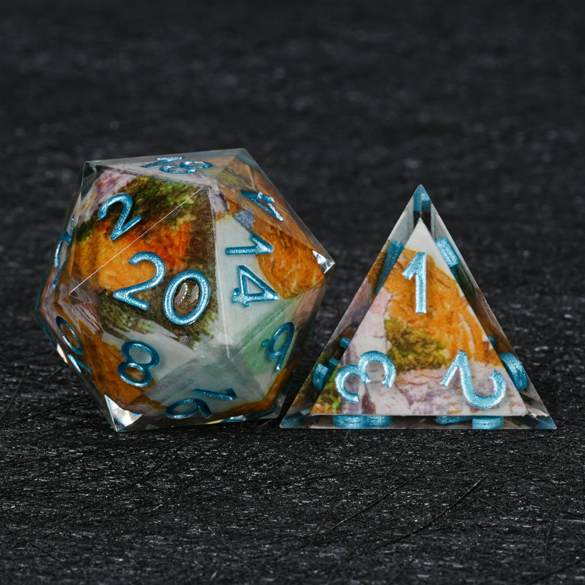 Resin D20 and pyramid-shaped D4 with orange and green autumn landscape artwork and metallic blue numbers