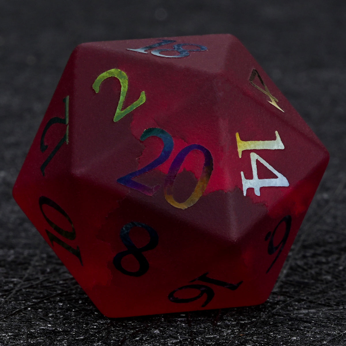 Garnet red frosted glass D20 die with rainbow-plated numbers, shown close up on a textured black surface