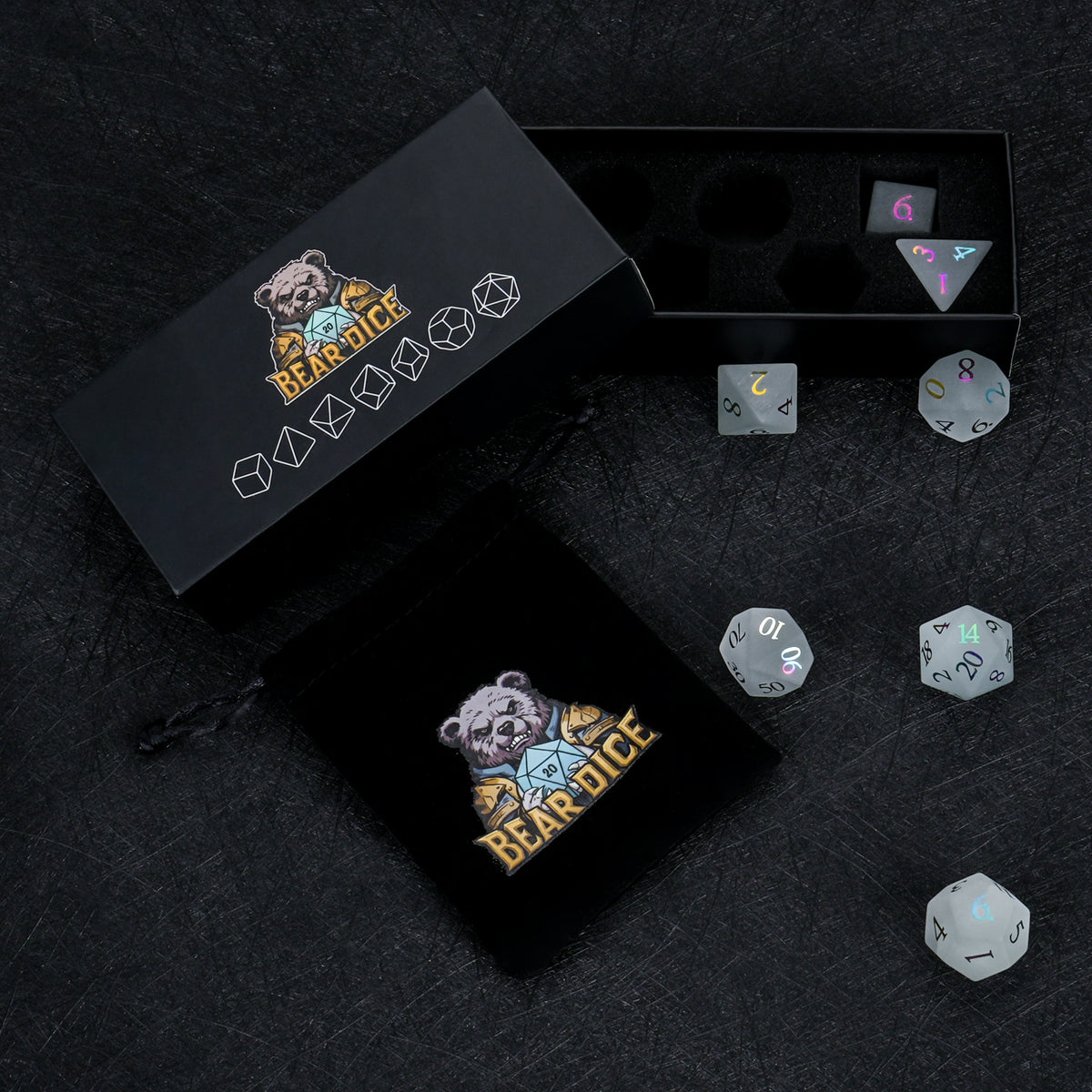 Gray frosted gemstone dice with multicolored electroplated numbers displayed beside black Bear Dice packaging boxes