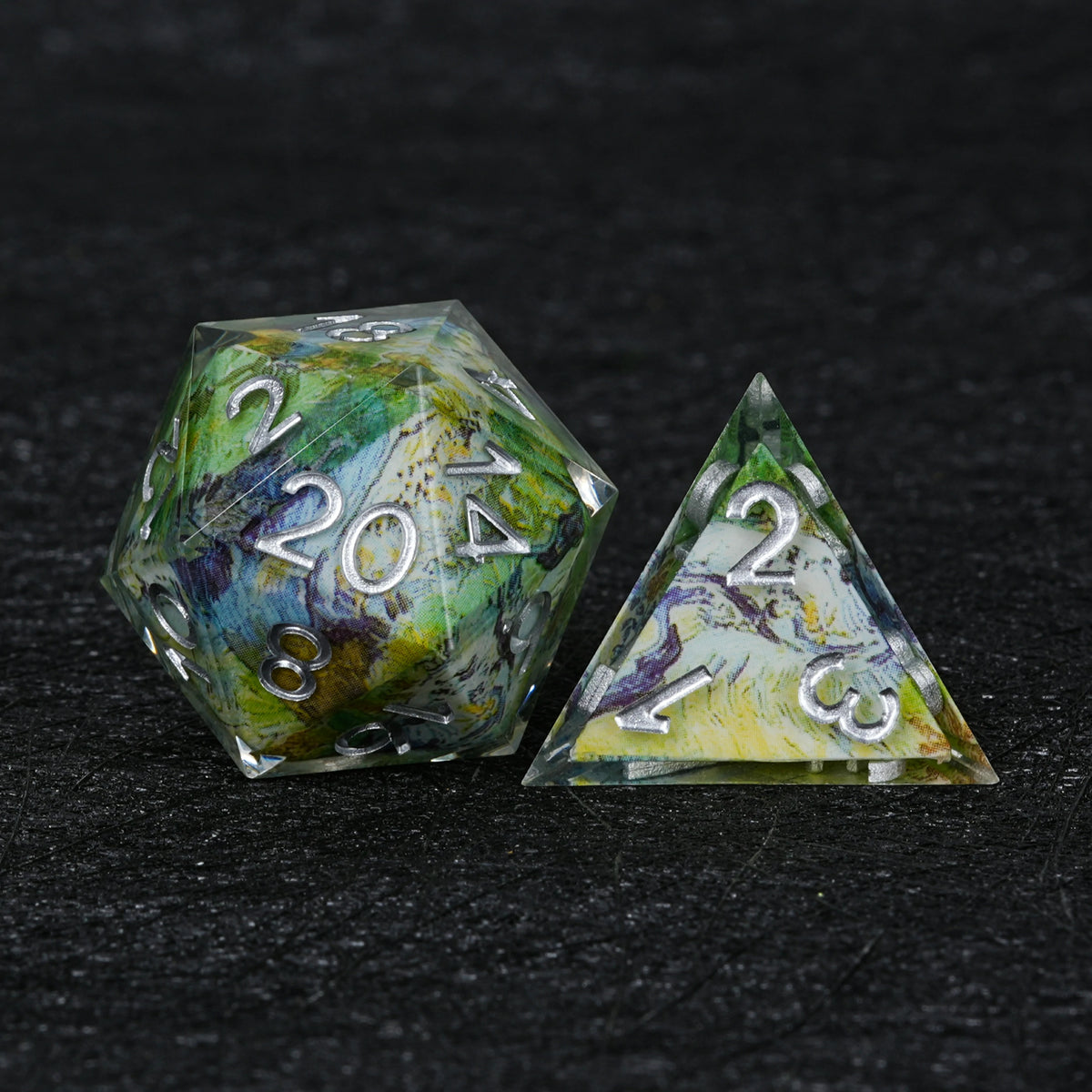 Close-up of a resin D20 with green, yellow, blue and white landscape decal artwork, silver-colored numbers and clear edges